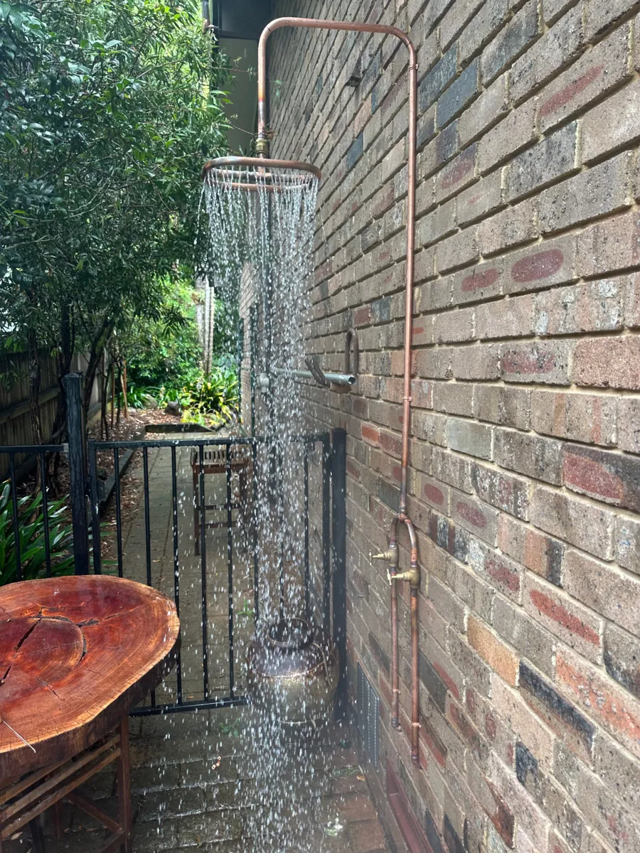 Custom copper outdoor shower running beside a brick wall