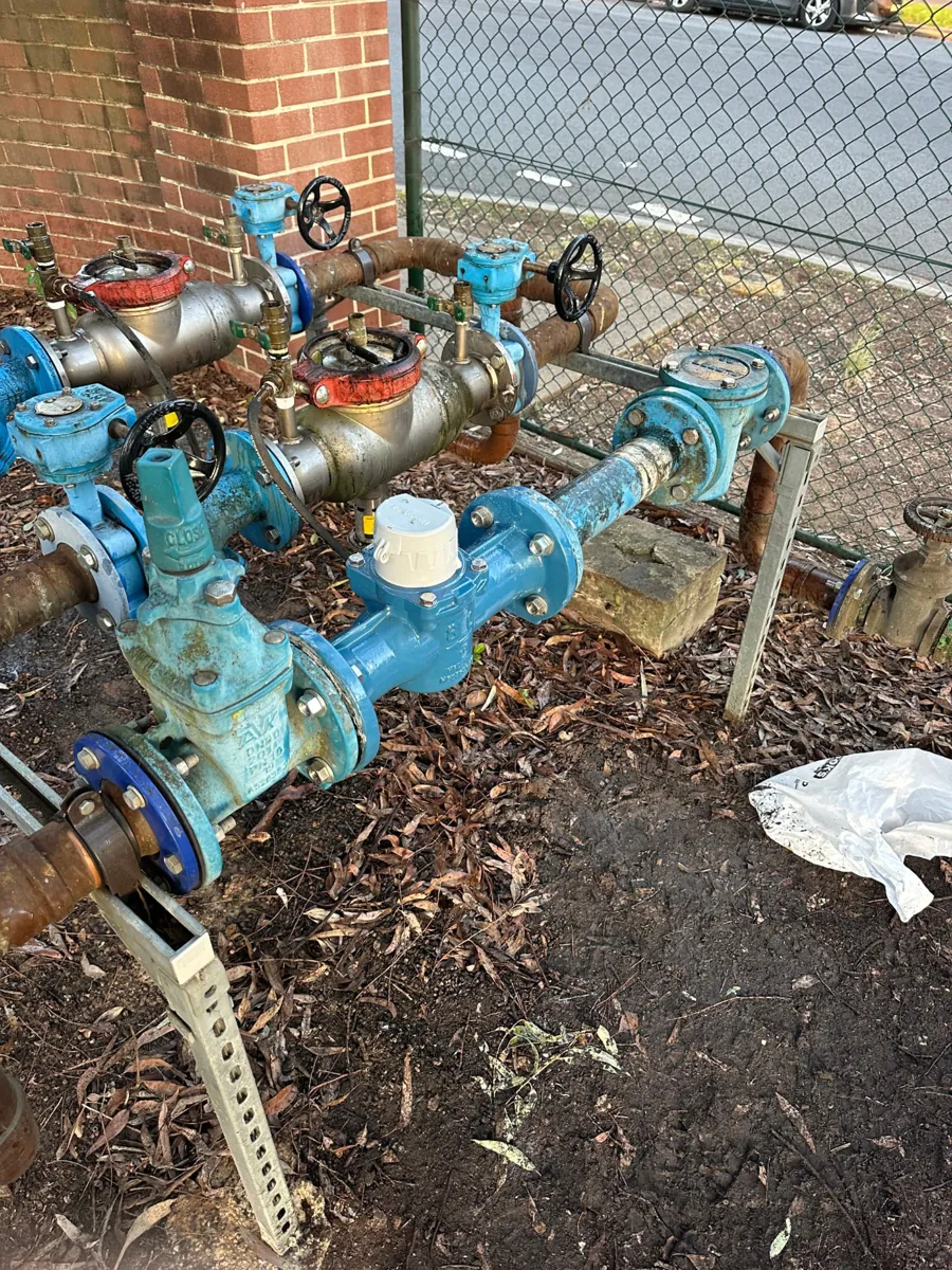Backflow prevention devices and water pipework beside a brick wall
